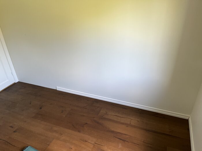 Listen längs väggen är för kort och når inte hörnet, vilket visas mot en vit vägg och ett mörkt trägolv.