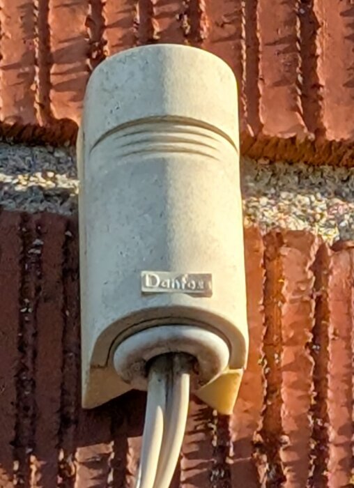 Givare på tegelvägg med logotypen Danfoss synlig, ansluten med två kablar.