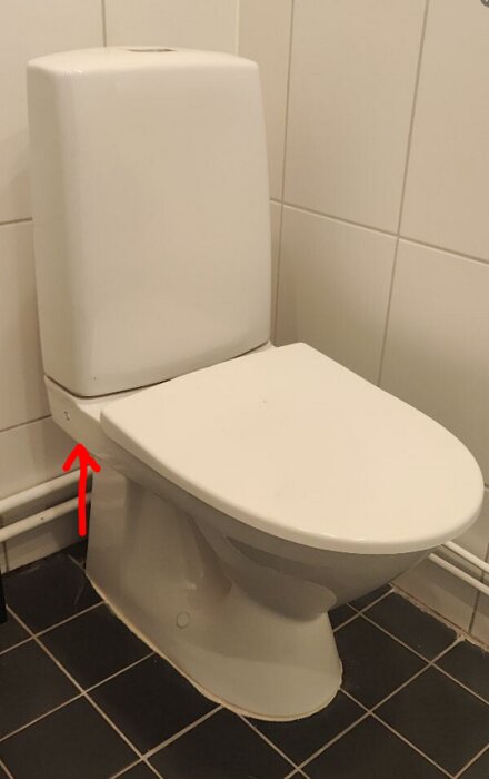 Toalett med en röd pil som pekar på sidan av cisternen där en skruv är placerad.