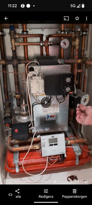 Värmeväxlare med kopparrör, tryckmätare och olika reglage inuti ett skåp, med en hand justerande en komponent.