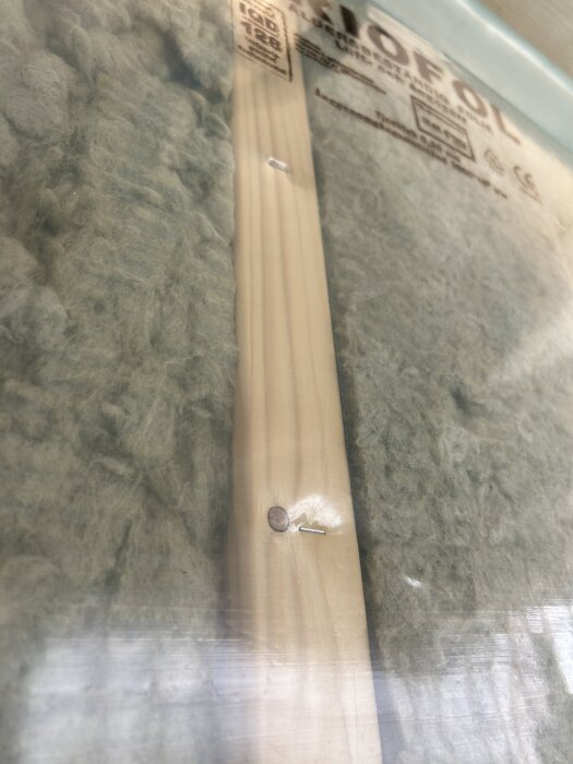 Isolering med plastfolie fäst med stift över en träregel.