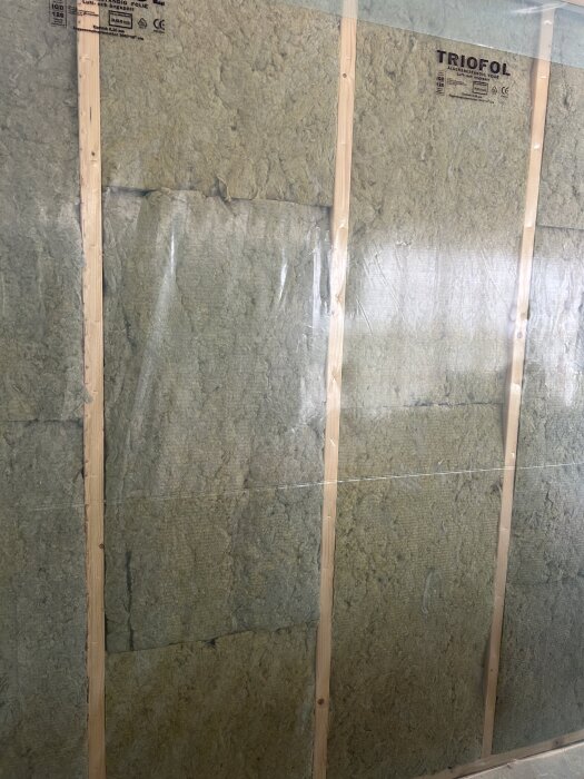 Väggisolering med plastfolie och träreglar, synliga stift håller plasten på plats.