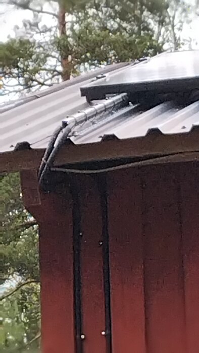 Kabeldragning över ett plåttak, med kablarna fästa längs kanten på ett hus i skogen.