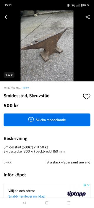 En smidesstäd i metall står på en asfalterad yta, omgiven av utomhusmiljö.