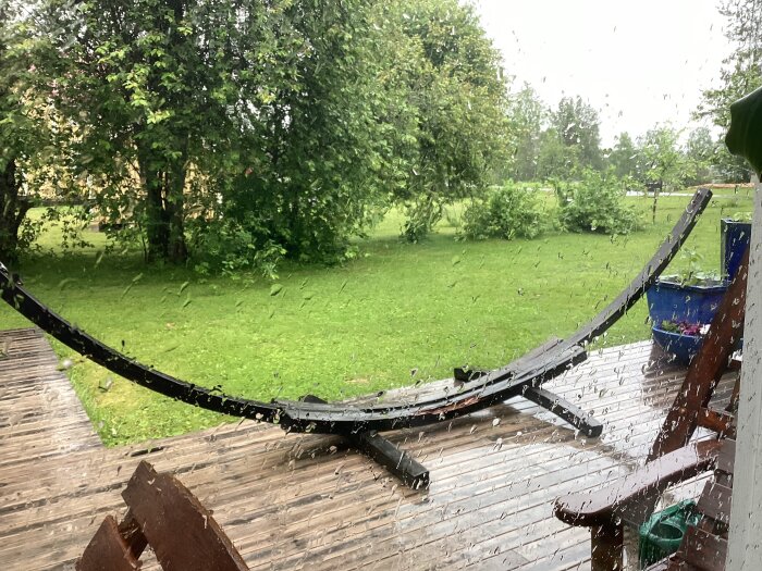 Hängmatteställning i regnigt väder på träaltan, med grön gräsmatta och träd i bakgrunden.