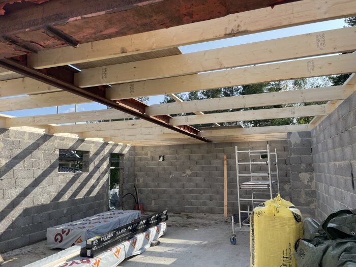 Pågående byggprojekt med synliga träbjälkar och väggar av betongblock. Stege och byggmaterial syns inuti strukturen.