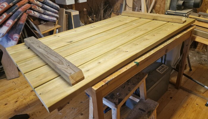 Träbord under konstruktion, ligger på arbetsbänk i verkstad med verktyg och material runtomkring.