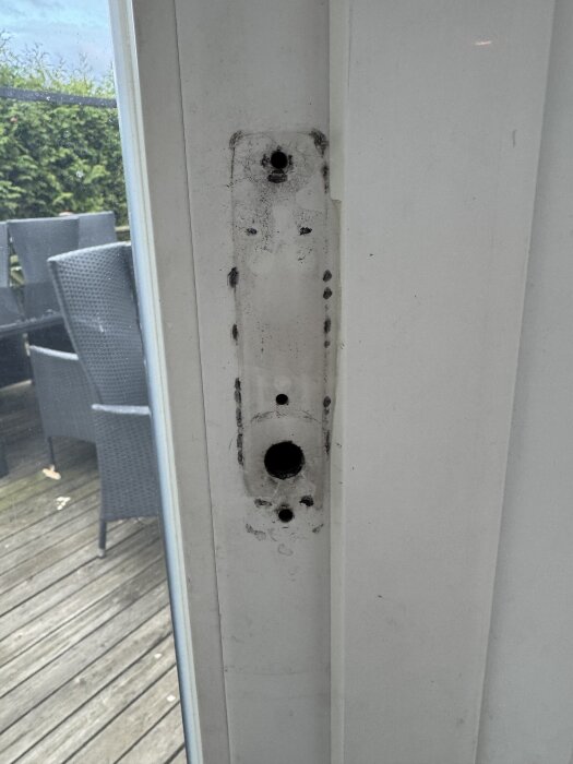 Slitet dörrhandtagsfäste på en altandörr med två små skruvhål längst ner och högst upp i en aluminiumram, omgiven av smutsmärken.