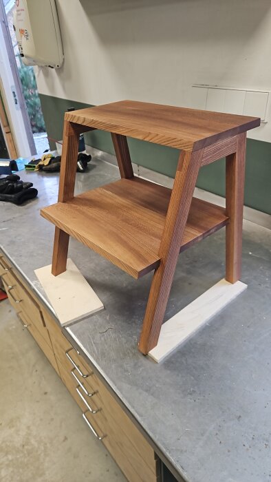 Barnpall av almträ, uppställd på en arbetsbänk i verkstaden, tillverkad med handverktyg, visar snygga fogar och trästruktur.