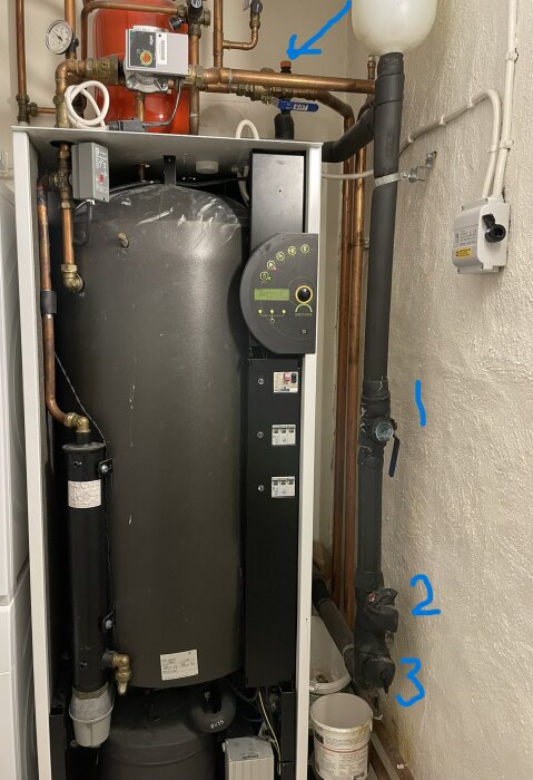 Värmepump IVT Greenline C5 med plaströr, kopparrör och ventiler markerade med blå streck och pilar. Brun vägg i bakgrunden.