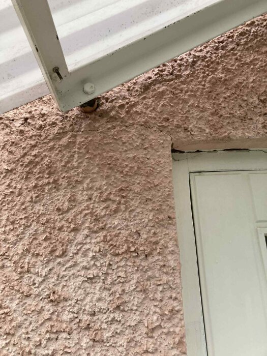 Putsad fasad på ett hus med synliga sprickor runt en dörr och under en vit taklist.