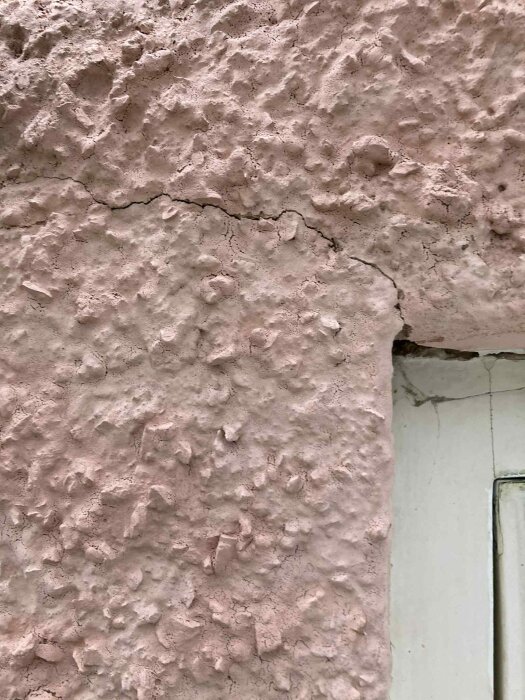 Spricka i putsad fasad vid ett husfönster, tecken på potentiellt behov av renovering.
