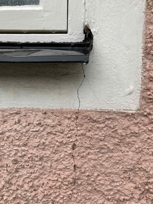 Spricka i putsad fasad vid ett fönster, med skador runt fönsterkarmen.