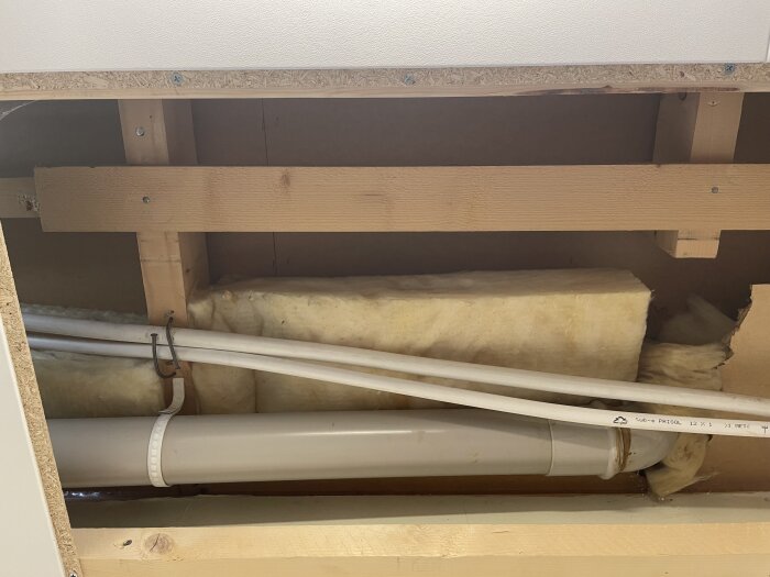 Isolerade rör samt träreglar bakom tvättstugans takpanel från ett hus byggt 1973. Bilden visar rörinstallation ovanför tvättstugan.