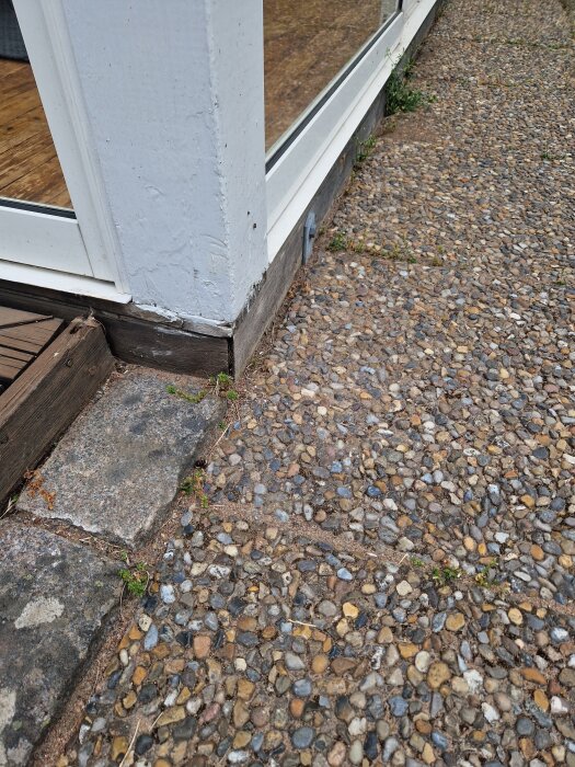 Omålat trä vid botten av en inglasad altan mot en stenbelagd yta.