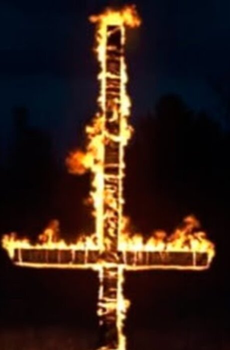En brinnande konstruktion i form av ett kors upp och ner, tagen vid en grillfest på natten.