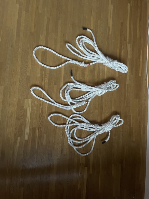 Tre vita förtöjningslinor i olika längder med krympslang i ändarna, placerade på ett trägolv.