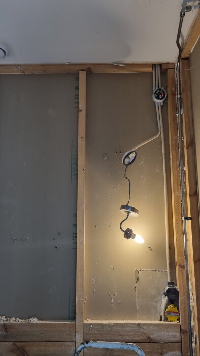 WC under renovering med borttaget kakel, exponerade kablar och väggmonterad lampa.