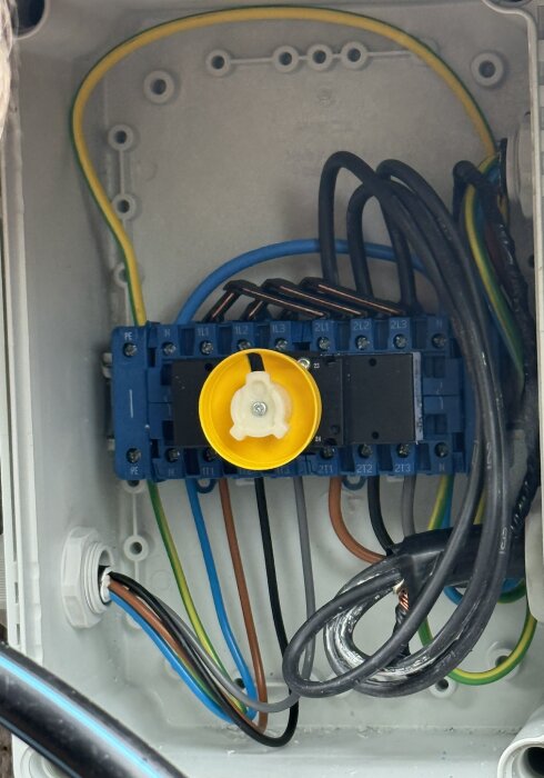 Elcentral med kablar anslutna till blå kopplingsplintar, gul centrumratt i mitten, omgiven av olika färgade kablar.