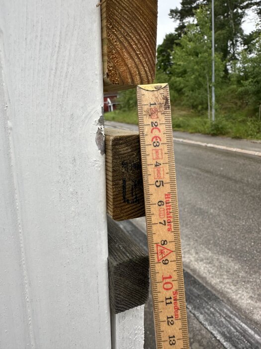 Måttstock visar avstånd på trästaket med bytta ribbor, cirka 60 cm cc mellan skruvreglarna.