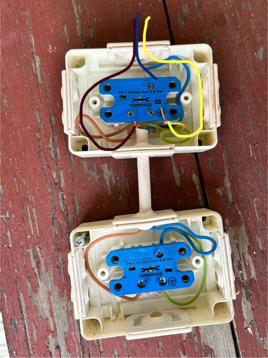 Två eluttag monterade på en trälila yta, med koppar- och flerfärgade kablar anslutna till blå kopplingsplintar.