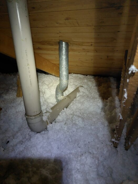 VVS-rör i en vind fylld med isoleringsmaterial, belyst av en ficklampa.