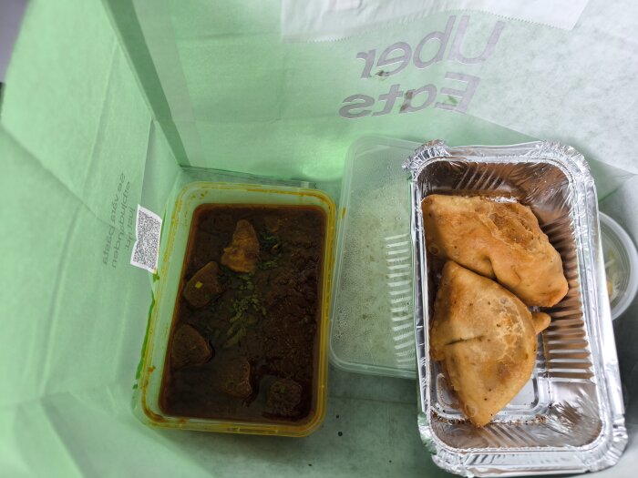 Indisk hämtmat i en påse med currykyckling i plastburk och två samosor i en aluminiumform från Upplands Väsby.