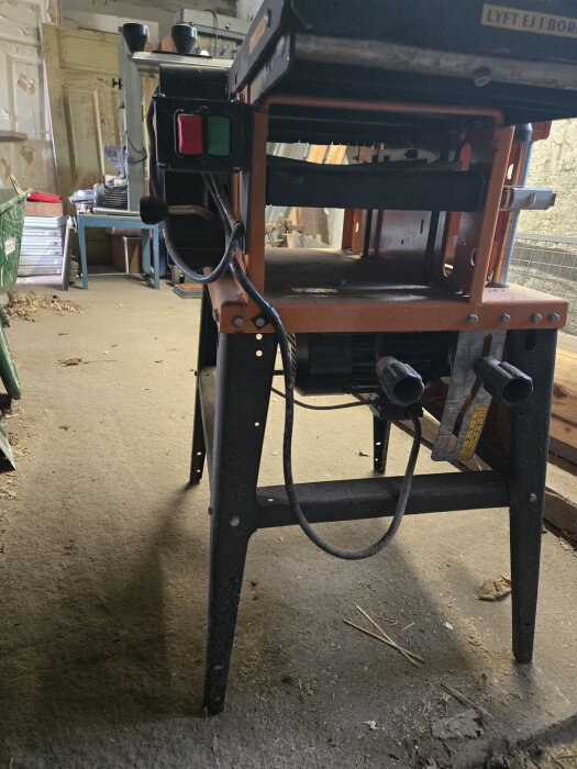 Verktygsmaskin i ett garage med sladd och strömbrytare synliga.