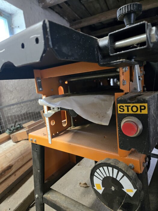 En snickerimaskin med en röd stoppknapp och justeringsratt i en verkstadsmiljö.