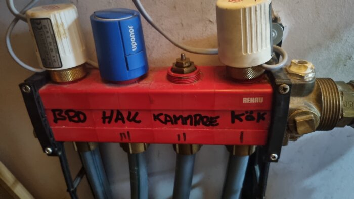 Röd fördelare med reglerventiler och anslutningar, text "BRO HALL KAMMARE KÖK" synlig, saknar en reglerventil med 20 mm gänga.