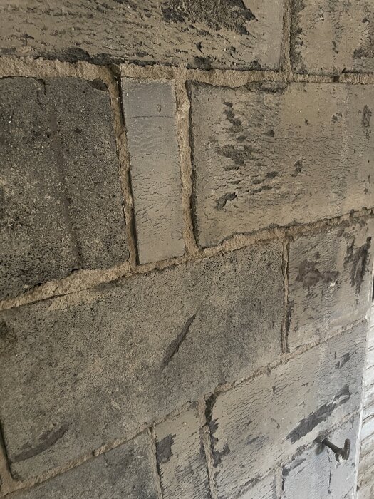 Vägg av betongblock med skrovlig yta, redo att putsas. En bult syns på ytan.