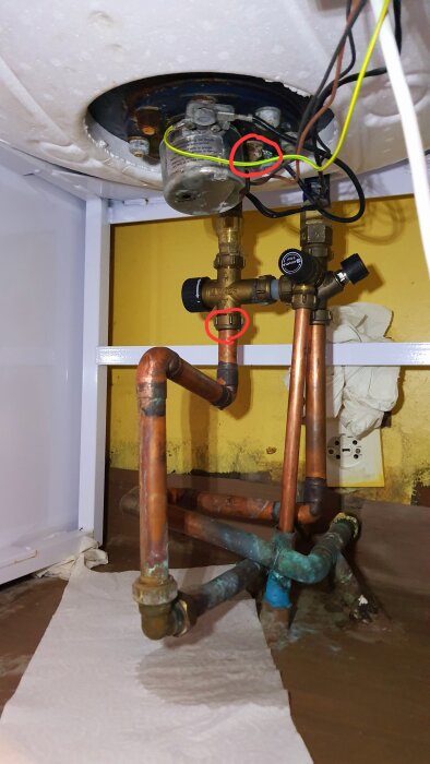 Rostig varmvattenberedare från 2003 med läckage, markerade platser där droppar uppstår. Kopparrör anslutna under. Papper absorberar vatten på golvet.