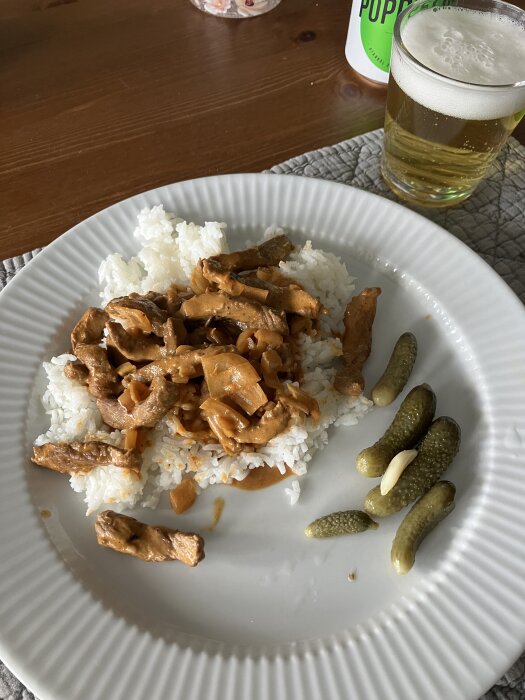 Tallrik med stroganoff på ryggbiff, ris och cornichons, öl i bakgrunden.