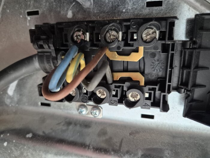 Närbild på elektrisk kopplingsplint med flera ledningar i olika färger anslutna, monterad i en metallram.