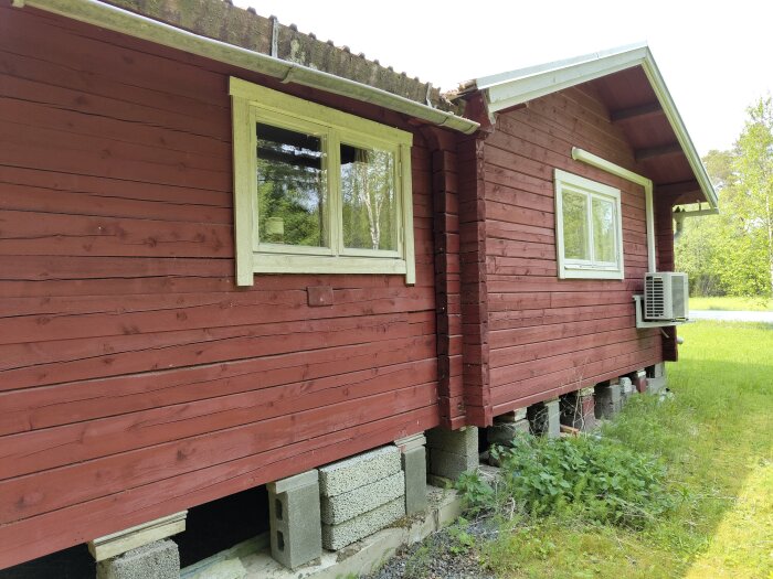 Röd sommarstuga med vita detaljer, visar en takränna utan takfotplåt ovanför ett hörnfönster där vatten har läckt in.