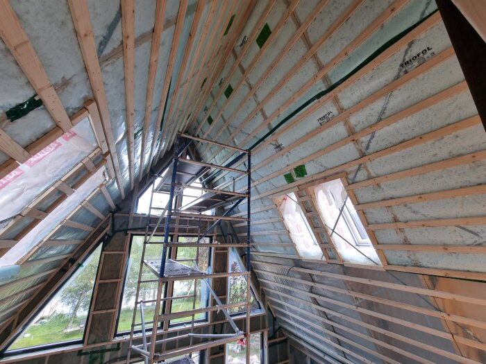 Ett rum under takrenovering med träreglar, plast och byggställning, förberett för mer sprutisolering.