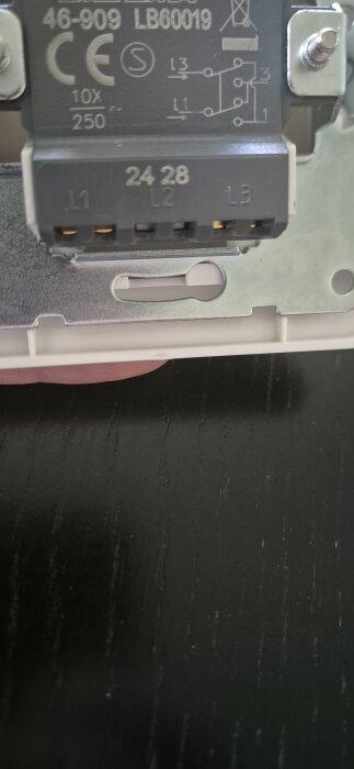 Elektrisk komponent med märkning och kontaktdon, visande anslutningar L1, L2 och L3, monterad på en metallplatta mot en svart bakgrund.