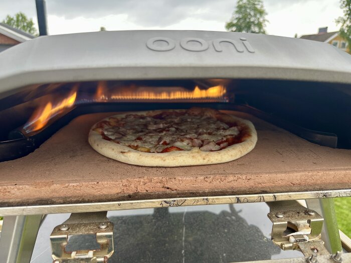 Pizza bakas i en utomhusugn med brinnande eld.