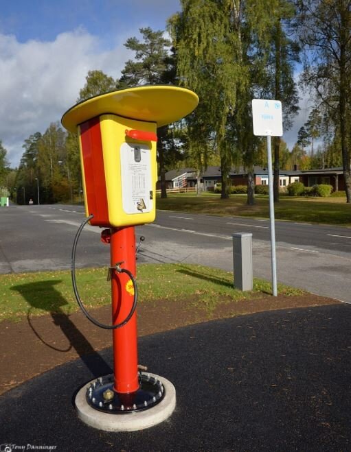 Gul och röd bensinautomat vid vägkant med skylt i bakgrunden, använd för tankning med enkronor.
