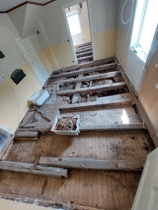 Rivning av golv i hus med synliga bjälkar och isoleringsmaterial. Brädor och delvis exponerade lager ses under renovering av familjehem.