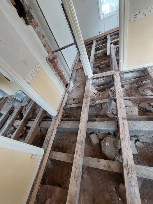 Renovering av torpargrund i hus, synliga golvreglar, gammalt murverk och jord under, konstruktion utan golvbeläggning.