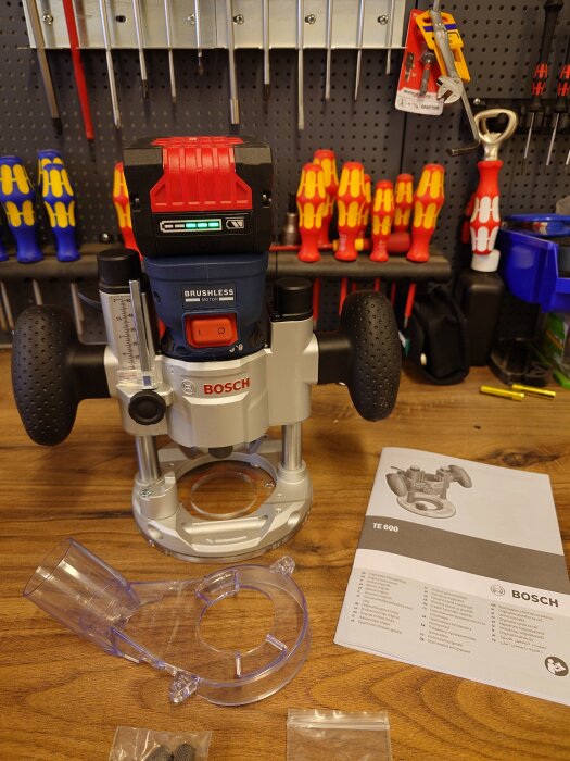 Bild av en Bosch TE 600 fräsenhet med tillbehör, monteringsmanual, och verktyg i bakgrunden på ett arbetsbord.