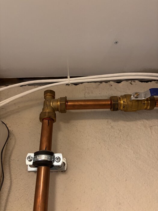 Kopparrör med mässingskopplingar och klämringar, monterade på en vägg i ett garage eller källare, del av ett VVS-system.