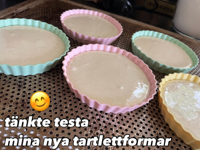 Sex tartlettformar i olika pastellfärger fyllda med smet på perforerad bakplåt. Texten "tänkte testa mina nya tartlettformar" visas.