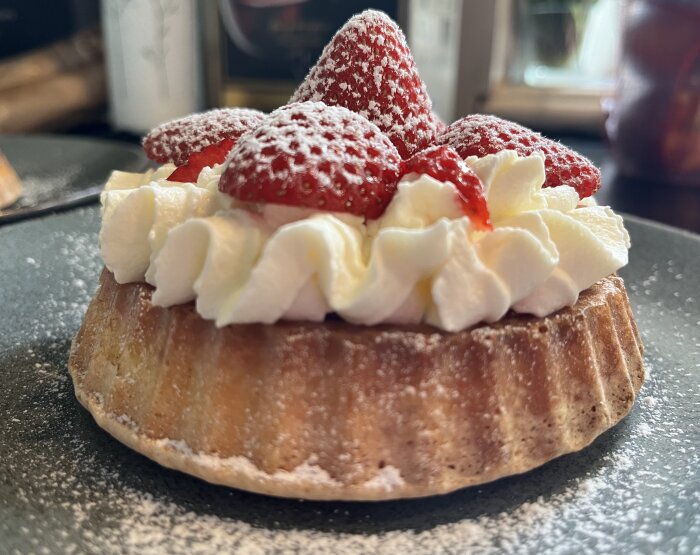 En bakelse med vispad grädde och färska jordgubbar på en tartlettbotten, pudrad med florsocker.