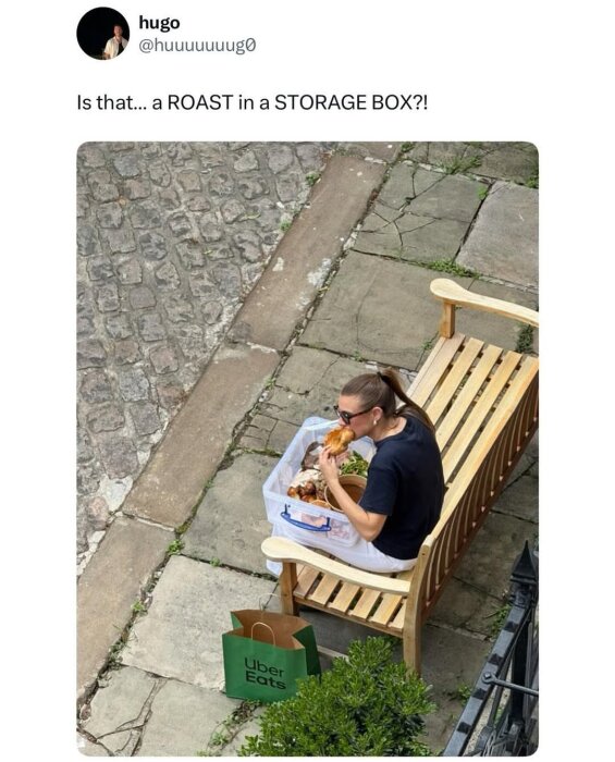 Kvinna sitter på en bänk och äter mat från en genomskinlig förvaringslåda. En Uber Eats-påse står på marken bredvid henne.