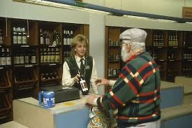 En man handlar vin över disk i en äldre Systembolaget-butik med en kvinnlig expedit bakom disken.