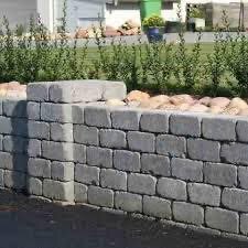 Grå stenmur av Benders Labyrint Maxi-stenar, del av landskap med buskar och stenarrangemang i bakgrunden.