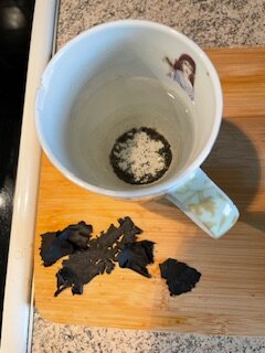 Svart färgflagor från yttertaket ligger bredvid en vit kopp på en träskärbräda.