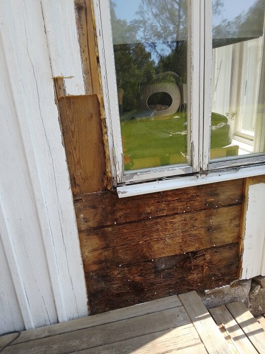 Fuktskadad träfasad under löst hängande fönster på gammalt torp. Flagnande färg och exponerat trä som behöver bytas ut.